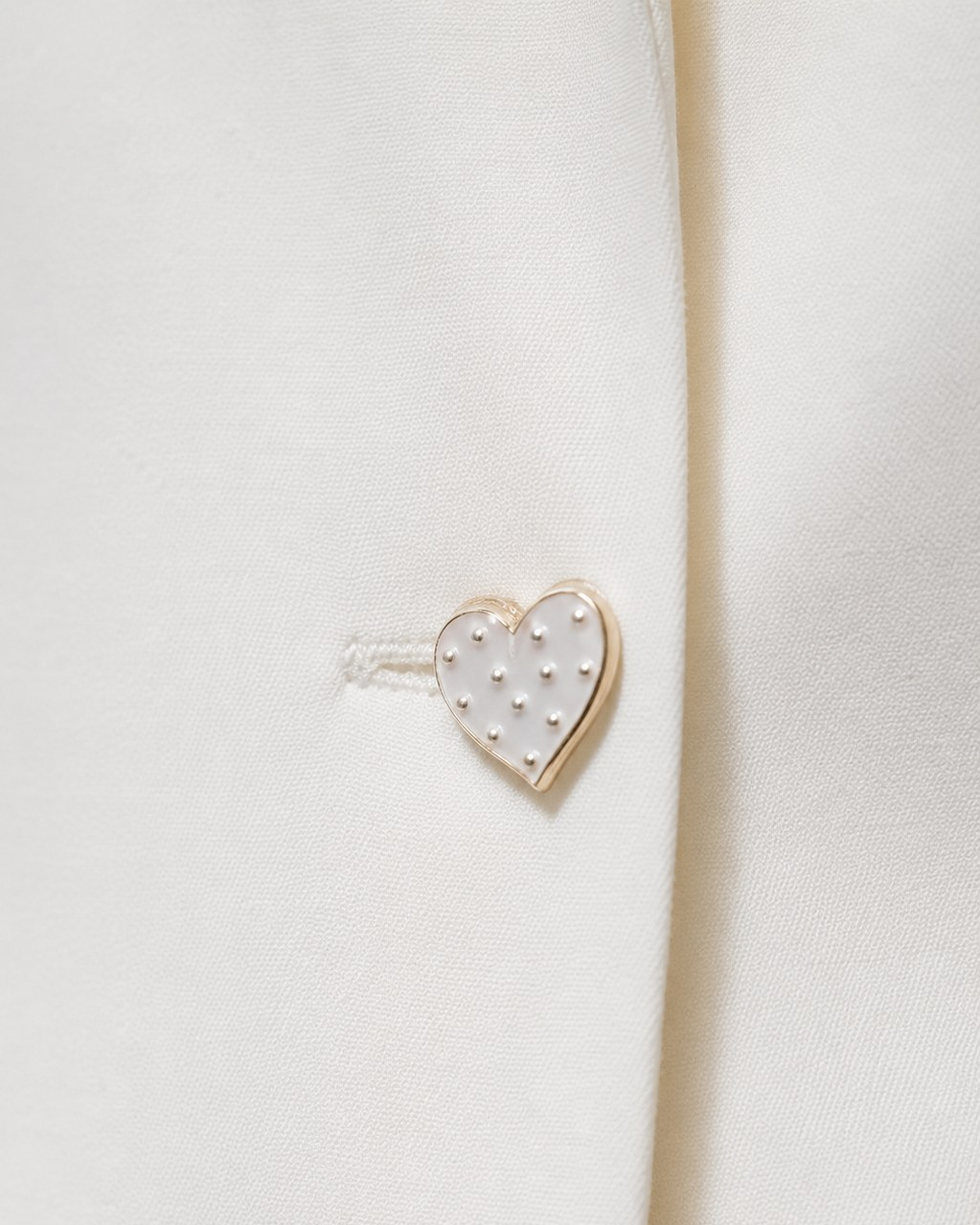 Close-up of heart-shaped pearl-detail button on ivory white blazer | Beyond Formals