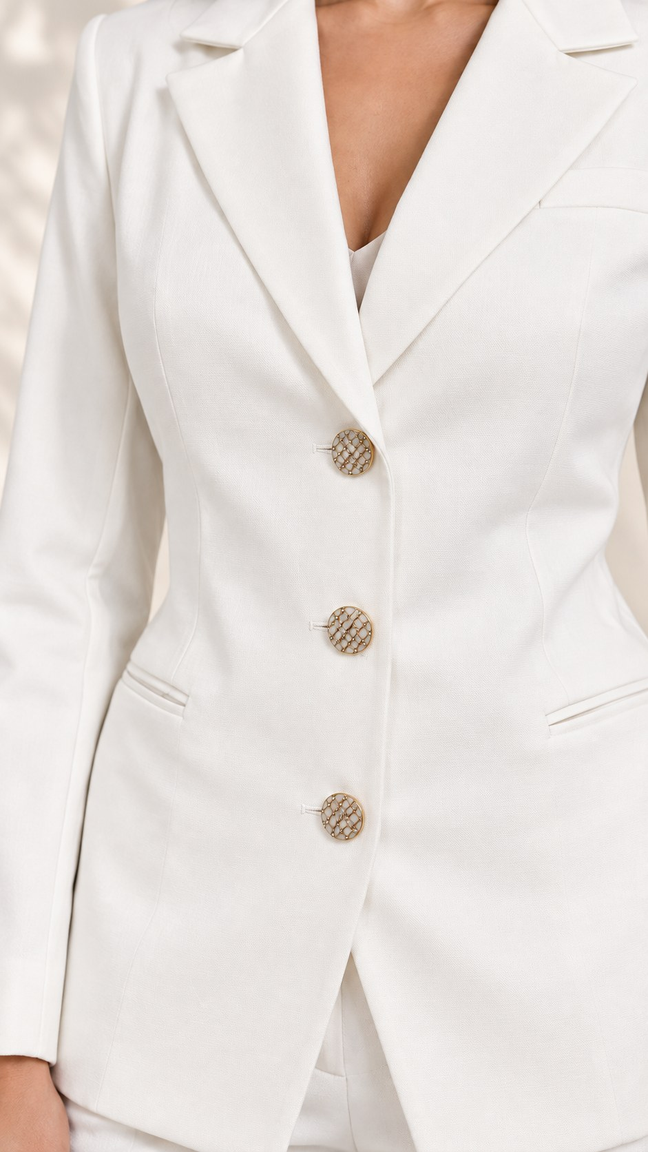 Close-up of white blazer textured gold-tone statement buttons and waist-defining seams | Beyond Formals