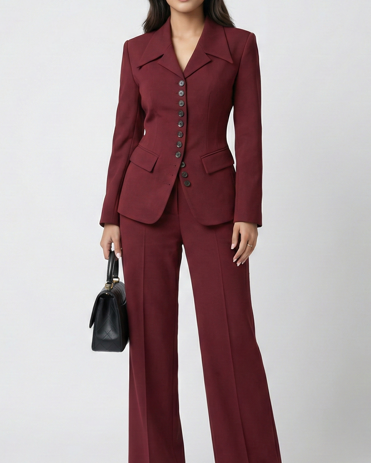 Woman wearing a burgundy suit holding a black handbag on a white background