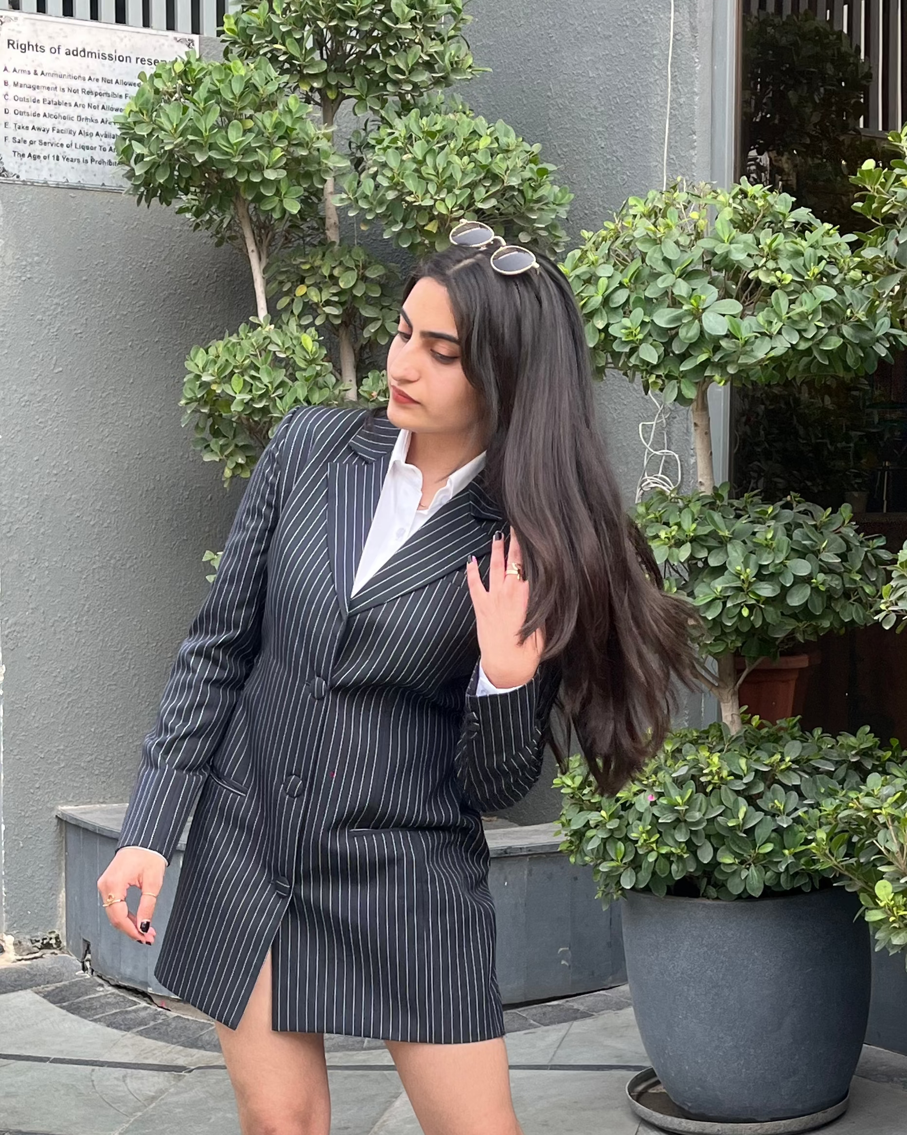 Woman in a pinstripe suit and white boots standing outdoors with plants in the background