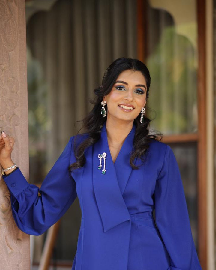 Woman in a blue outfit standing against a textured wall.
