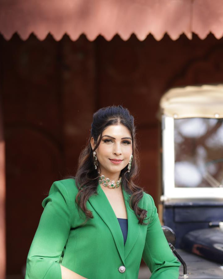 Woman in a green suit standing next to an old-fashioned vehicle with a blurred background