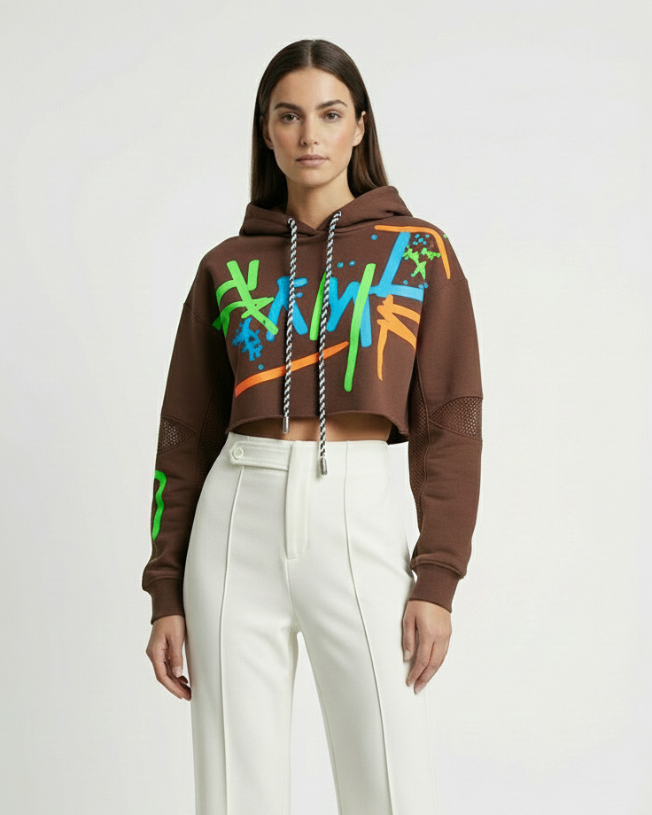 Person wearing a brown hoodie with colorful designs and white pants on a white background