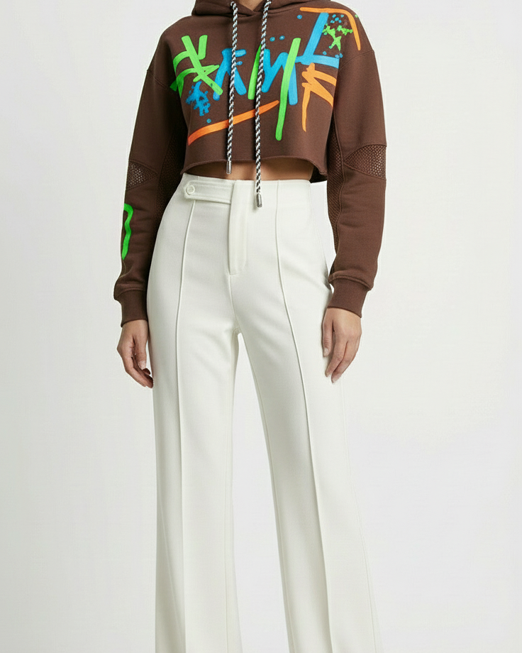 Person wearing a brown hoodie with colorful designs and white pants on a white background