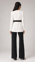 Woman wearing a white blazer with a black belt and black pants on a gray background
