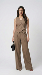 Woman wearing a brown vest and pants set with a black handbag on a white background