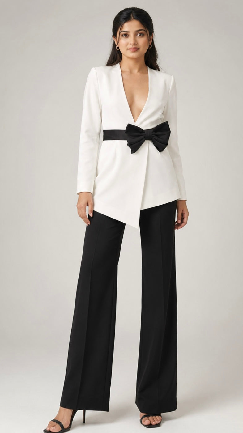 Woman wearing a white blazer with a black bow tie and black pants on a gray background