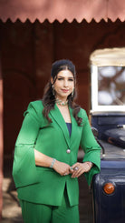 Woman in a green suit standing next to an old-fashioned vehicle with a blurred background